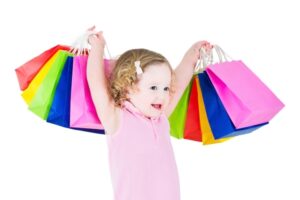 Cute little girl showing colorful shopping bags, isolated on white